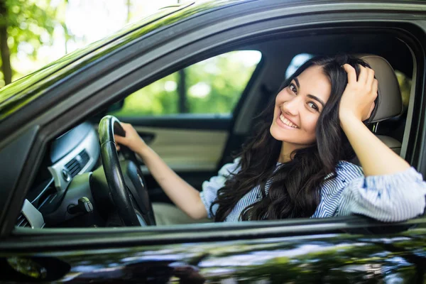 Bonita mulher motorista sorrindo para você de seu carro na rua — Fotografia de Stock