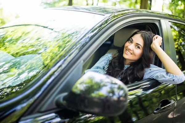 Wanita muda mengendarai mobil di kota. Potret seorang wanita cantik di dalam mobil, melihat ke luar jendela dan tersenyum . — Stok Foto