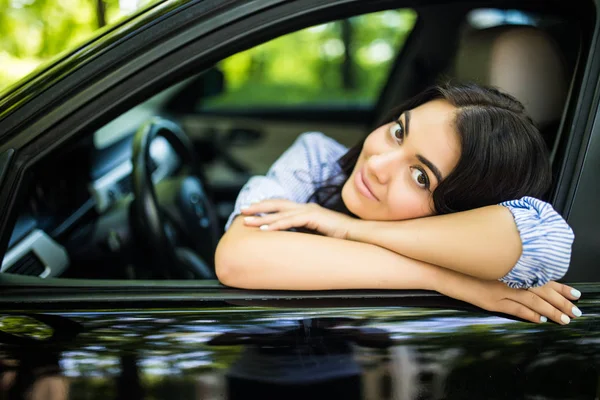 Красивая молодая женщина сидит внутри автомобиля, улыбаясь, опираясь на открытое окно — стоковое фото
