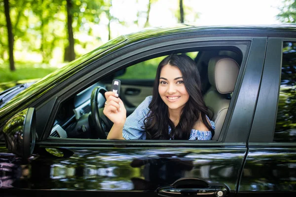 Wanita muda yang bahagia pemilik mobil baru tersenyum dan menunjukkan kunci di kursi pengemudi — Stok Foto