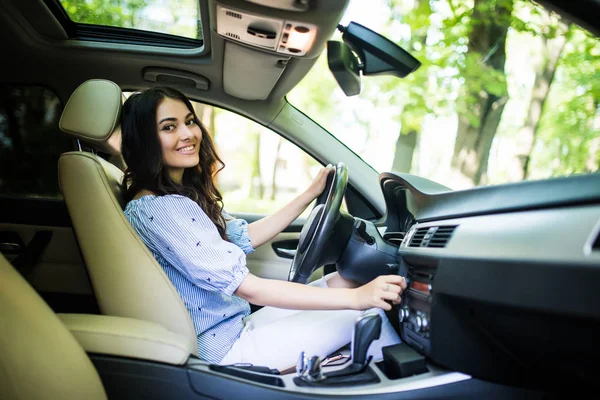 Jonge lachende vrouw bestuurder met eigendom veiligheidsgordel inschakelen of tuning voertuig audio, het vinden van een afspeellijst voor een aangename en comfortabele rit. — Stockfoto