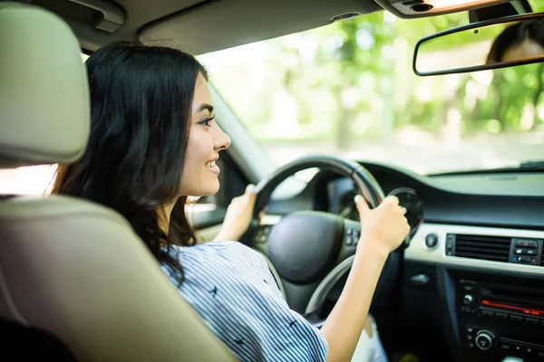 Visão traseira da jovem mulher atraente em desgaste casual olhando sobre o ombro enquanto dirige um carro — Fotografia de Stock