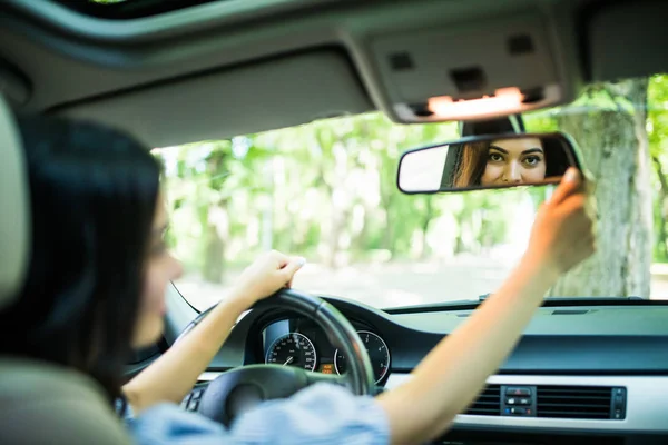 Wanita muda menyentuh kaca spion dan tersenyum sambil mengendarai mobil — Stok Foto