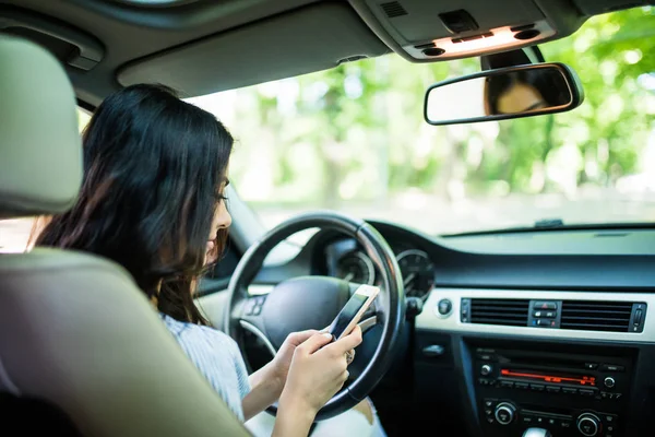 Jovem mulher de beleza olhando para o smartphone enquanto dirige a visão traseira do carro — Fotografia de Stock