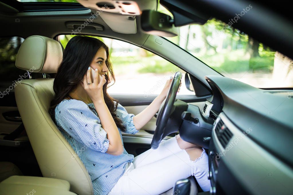 Young woman driving car and talking on cell phone concentrating on the road