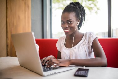 Kahve Dükkanı, kulaklık müzik dinleme favori dinlenme ve ağlarda sohbet neşeli kadın siyah modeli. Dizüstü bilgisayarda çalışma güzel koyu tenli serbest meslek