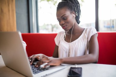 Dizüstü bilgisayar ile restoranda oturan genç Afrikalı-Amerikalı kız. Sevinçle kafede dizüstü seyir kulaklık ile güzel kız.