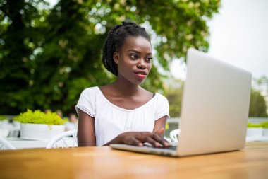 Güzel genç siyah kadın girişimci sokak barda oturmuş ve Uzaktan laptop ile onun proje üzerinde çalışma. Çekici Afro-Amerikan bağımsız kız netbook ile açık kafede oturuyor