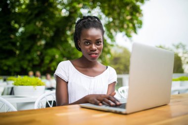 Güneşli bir günde dışarıda kafede dijital tablet ile çalışan genç afro Amerikan siyah kadın serbest meslek.