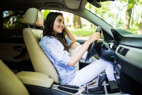 Mujer joven mirando por encima de su hombro mientras conduce un coche — Foto de Stock