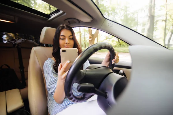 Молодая женщина пользуется телефоном за рулём своей машины — стоковое фото