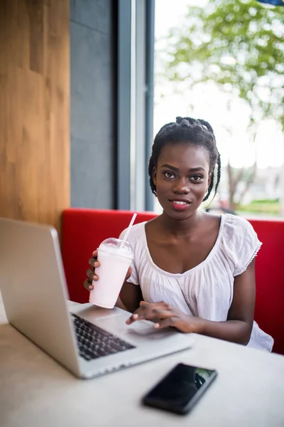 Mujer afroamericana joven relajante, navegar en el ordenador portátil de Internet, beber batido en la cafetería — Foto de Stock