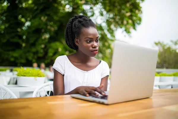 Afro americano joven negro rizado hembra está sentado en la cafetería y tener trabajo remoto utilizando el ordenador portátil — Foto de Stock