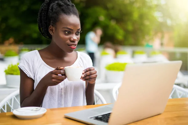 Encantadora joven empresaria afroamericana está sentada en el restaurante de la calle y tiene una sesión de video en línea remota con colegas que usan computadora portátil, cálido día soleado — Foto de Stock
