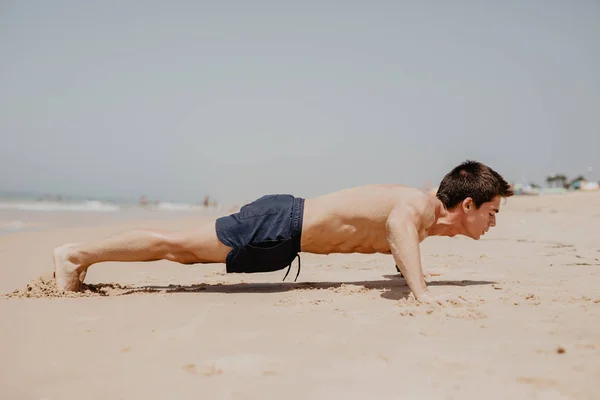 Фитнес человек осуществляет отжимания улыбаясь счастливым. Мужская фитнес-модель  кросс-тренировки на пляже . — Спорт, Мышцы - Stock Photo | #162218944