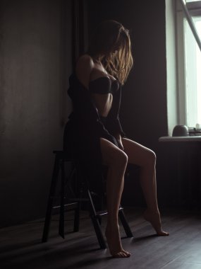 Baştan çıkarıcı, güzel ve çekici genç kadın gevşek kahverengi saçlı, seksi şekilli rakam ve siyah dikişsiz iç çamaşırı ve yün ceket uzun bacaklar stüdyoda sandalyede poz