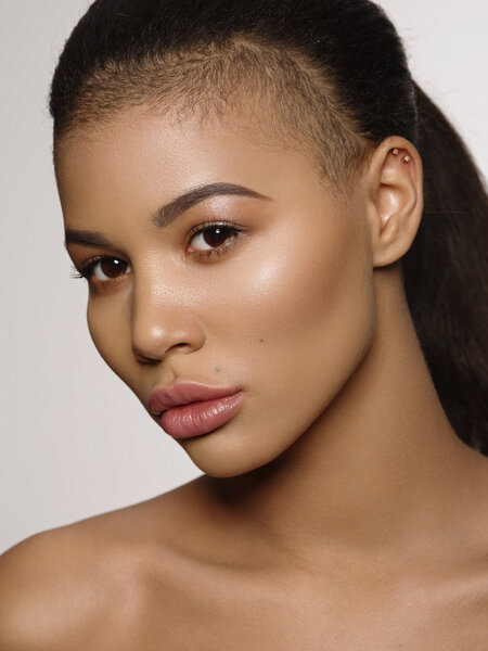 Fashion portrait of an extraordinary beautiful african american young woman with perfect smooth golden skin, full lips and shaved haircut, studio shoot, light background