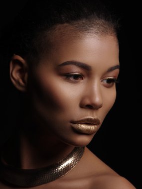 Bir olağanüstü güzel çıplak Afro-Amerikan model mükemmel pürüzsüz parlak melez deri, makyaj, tam altın dudaklar, traş saç kesimi ve boynunu koyu arka plan üzerinde altın takı ile portresi
