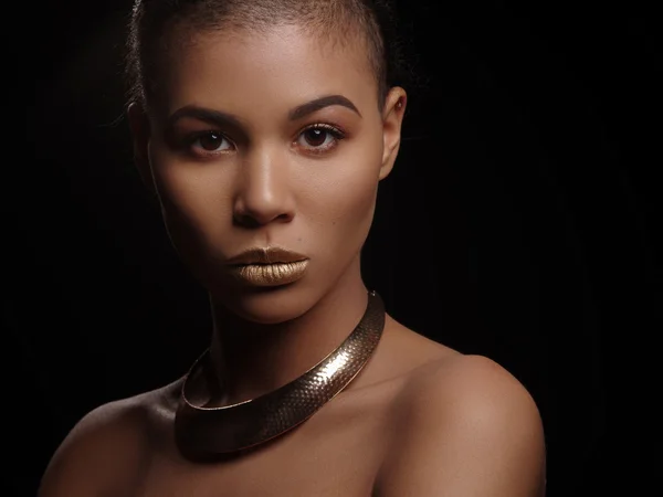 Fashion portrait of a beautiful naked african american woman with perfect smooth glowing mulatto skin, make up, full golden lips, shaved haircut and gold necklace, studio shoot