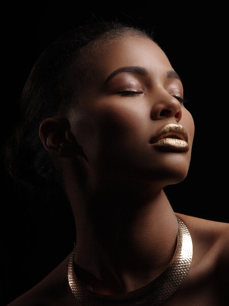 Fashion studio portrait of an extraordinary beautiful nude african american woman with perfect smooth glowing mulatto skin, make up, full golden lips, shaved haircut and gold necklace, profile