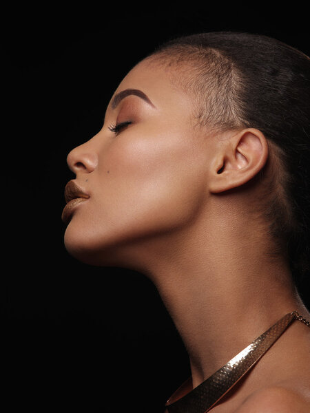 Fashion studio portrait of an extraordinary beautiful nude african american woman with perfect smooth glowing mulatto skin, make up, full golden lips, shaved haircut and gold necklace, profile
