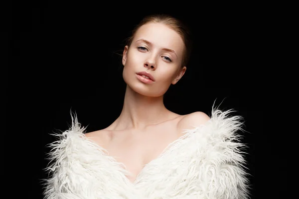 Una sensual y hermosa mujer joven con maquillaje desnudo en su perfecta cara brillante con un abrigo de piel artificial blanco de moda en el cuerpo desnudo está posando en el estudio — Foto de Stock