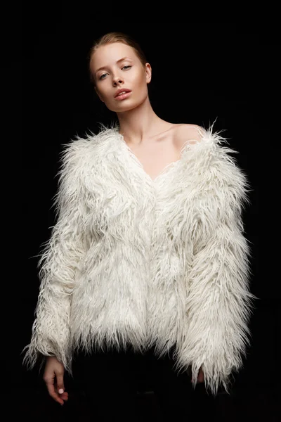 Una hermosa modelo sensual con maquillaje desnudo en su piel brillante perfecta está posando en el abrigo de piel artificial blanco de moda en el cuerpo desnudo en el estudio — Foto de Stock