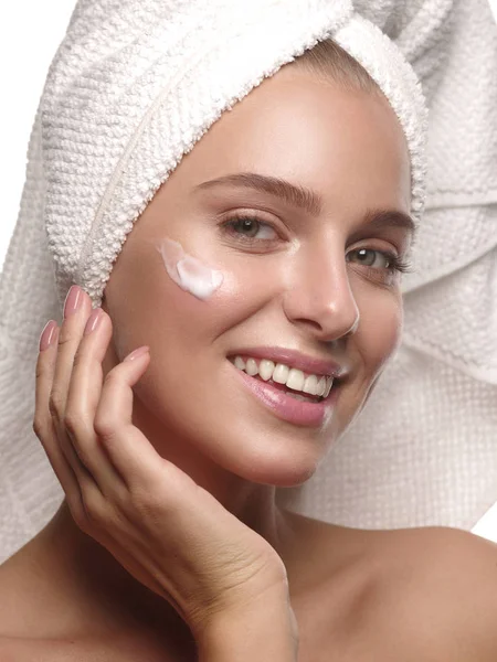 Portrait of a girl with pure and healthy glowing skin without makeup, who is doing daily skincare using moisturizing creme after shower with the towel on her head, wellness and spa, white background — Stockfoto