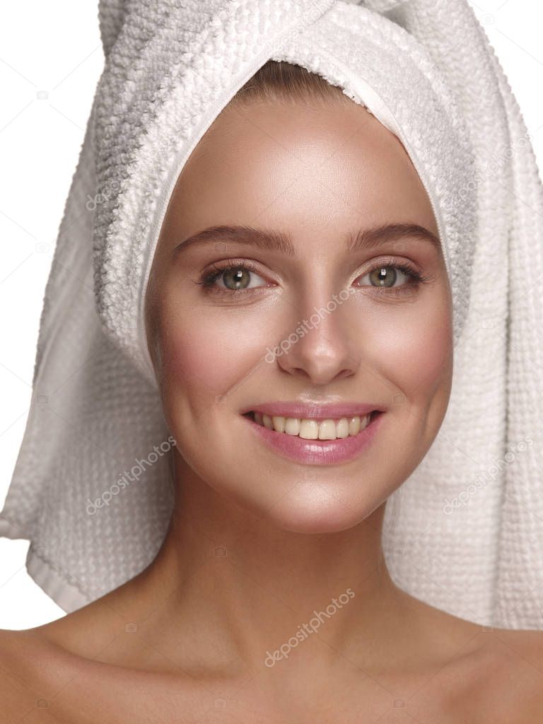 Portrait of a young girl with pure, healthy, smooth and natural glowing skin without any makeup, who is doing daily skincare after the shower with the towel on her head, white isolated background
