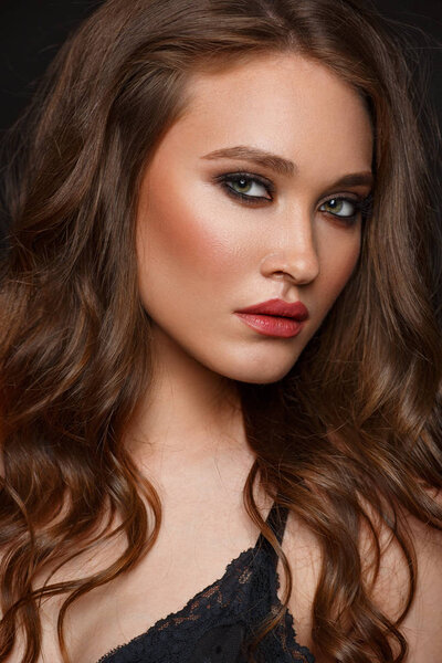 Studio portrait of a young bitchy and beautiful woman with long wavy hair and expressive makeup on the black background