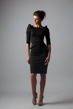 Moda, kendi kendine yeterli ve kendine güvenen genç kadın şık siyah elbise giyen toplanan saç ve makyaj, gri arka plan, studio fotoğraf ile