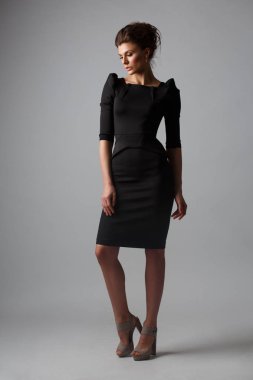 Güzel, kendi kendine yeterli ve kendine güvenen genç kadın şık siyah elbise giyen toplanan saç ve makyaj, gri arka plan, studio fotoğraf ile