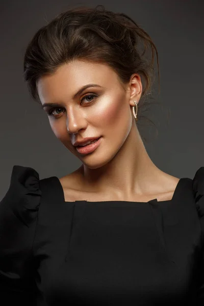 Portrett av en vakker, selvforsynt og selvsikker ung kvinne med innsamlet hår i elegant svart kjole med sminke, mørk bakgrunn, studiobilde – stockfoto
