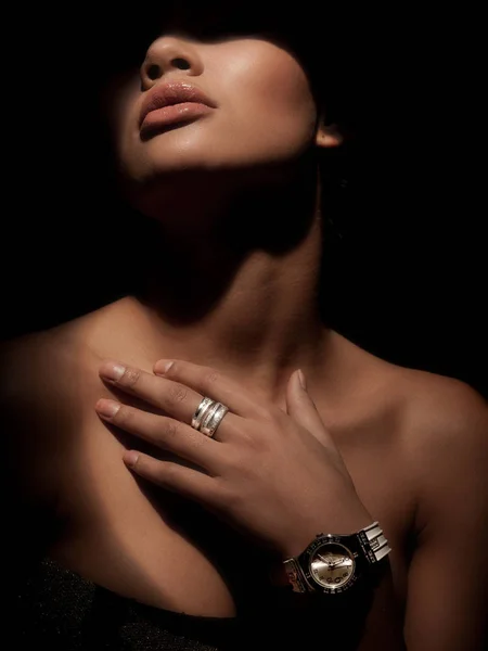 Retrato de una mujer elegante, hermosa y misteriosa con anillos anchos de lujo hechos de metales preciosos en su dedo y reloj en su muñeca. Fondo oscuro del estudio. Sombra en la cara. Elegancia . —  Fotos de Stock