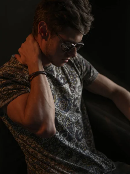 Atletik, seksi ve kendine güvenen adam anız sakal ve havacı güneş gözlüğü ile deri kanepede kapalı poz   