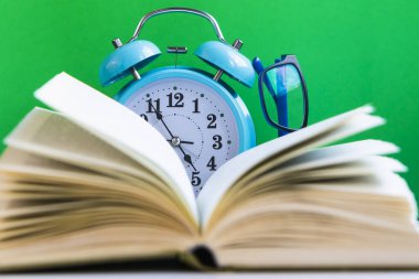 Yeşil arka planda çalar saat ve gözlüklü bir kitabı aç