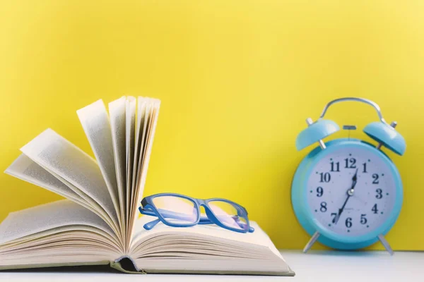 Open book with glasses and an old alarm clock.