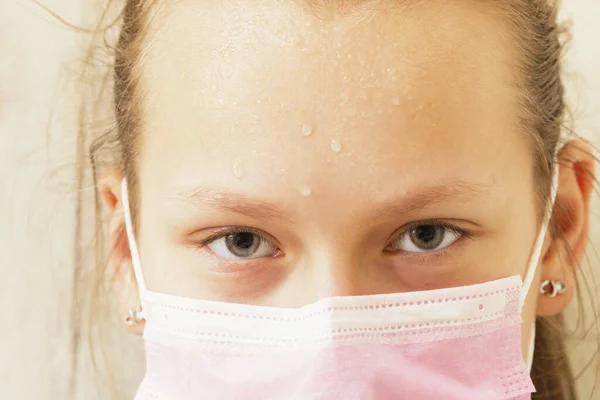 Tıbbi maskeli bir kızın alnında ter var.
