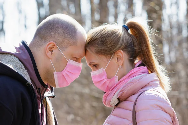 Man and woman in medical masks touch each other's heads in nature during quarantine
