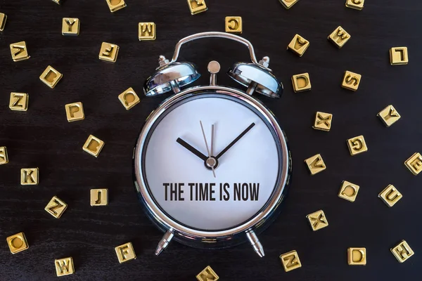 El momento es ahora - Reloj despertador en mesa de madera con letras —  Fotos de Stock