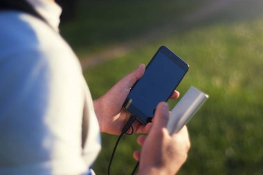 Adam bir taşınabilir şarj cihazı ile bir smartphone elinde tutuyor. Adam arka plan yeşillikleri ile doğanın üzerinde