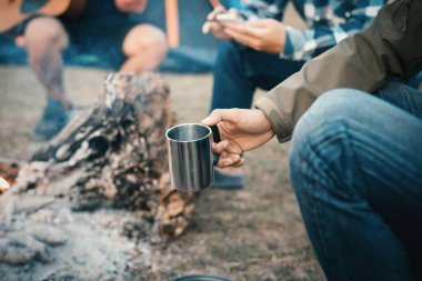 Man traveler hands holding cup of tea near the fire outdoors,Fri