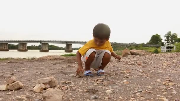 Lindo asiático pequeño niño jugando con piedra cerca río — Vídeo de stock