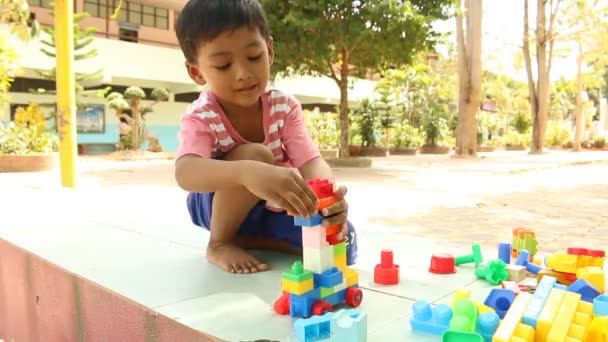 Kleine schattige Aziatische jongen spelen met kunststof gebouw blokkeert in het park — Stockvideo