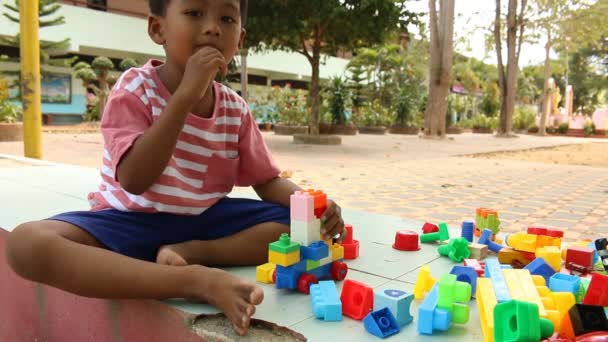 プラスチック ビルディングで遊んで少しかわいいアジアの少年が公園でブロックします。 — ストック動画