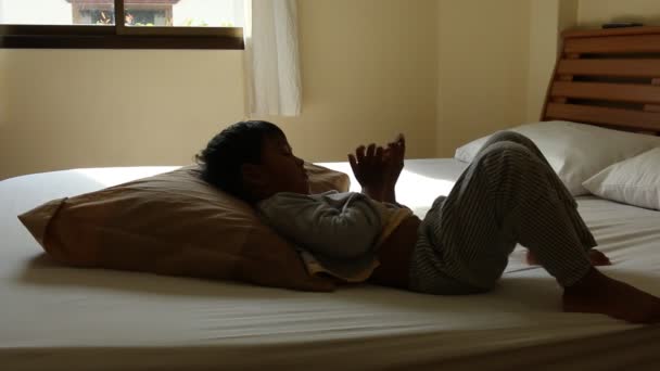 Милый азиатский мальчик лежит на кровати и слушает музыку на смартфоне — стоковое видео