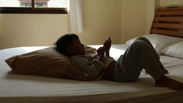 Bonito asiático menino deitado na cama e ouvir música no telefone inteligente — Vídeo de Stock