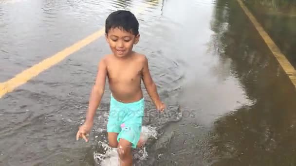 Feliz asiático menino jogar água na estrada, estrada inundada, depois da chuva pesada à noite — Vídeo de Stock