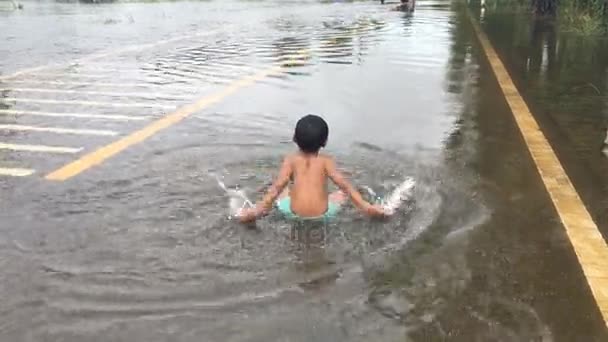 Glad asiatiska pojke spela vatten på vägen, översvämmade road, efter tunga regn i kväll — Stockvideo