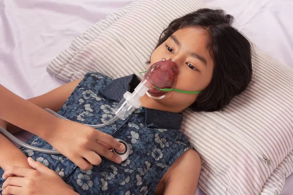 Girl sick in inhaler mask for kid lying on Patient's bed
